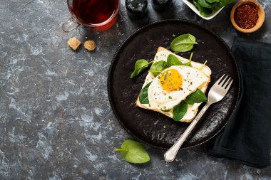 Toast with cream cheese, spinach and fried egg, top view.
