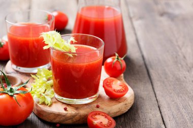 Tomato juice in glass with celery, cherry tomato on dark background.