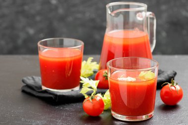 Tomato juice in glass with celery, cherry tomato on dark background.