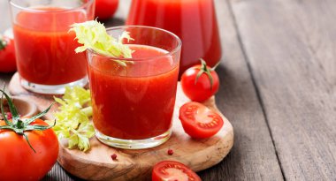Tomato juice in glass with celery, cherry tomato on dark background.