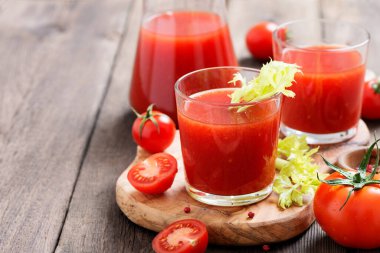 Tomato juice in glass with celery, cherry tomato on dark background.