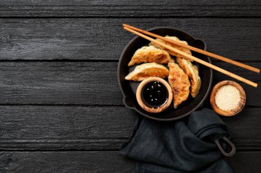 Fried dumplings Gyoza in a frying pan, soy sauce, and chopsticks on a black wooden background, top view