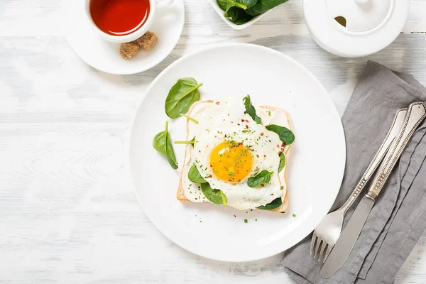 Toast with cream cheese, spinach and fried egg, top view.