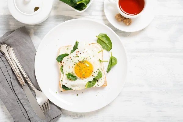 Toast with cream cheese, spinach and fried egg, top view.