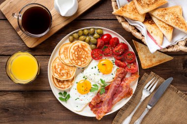 İki omlet, krep, domates salatası, domuz pastırması ve yeşil zeytinli Amerikan kahvaltısı. en üstteki görünüm
