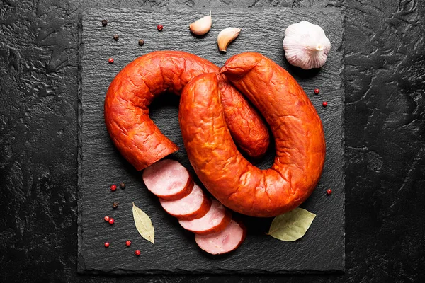 Smoked sausage ring with spices and herbs on black background. top view