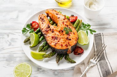 Beyaz tabakta ızgara somon bifteği kuşkonmaz ve kirazlı domates. Beyaz tahta arkaplan. 