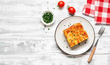 Eritilmiş peynirle kaplı ve gri tabakta servis edilen taze maydanozla süslenmiş kıymalı lazanya porsiyonu. Üst Manzara. Metin için boşluk