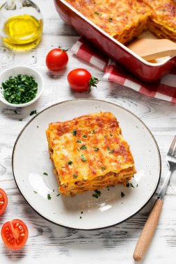 Eritilmiş peynirle kaplı ve gri tabakta servis edilen taze maydanozla süslenmiş kıymalı lazanya porsiyonu. .