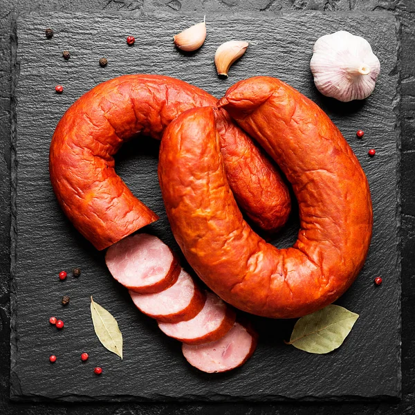 Smoked sausage ring with spices and herbs on black background. top view