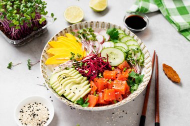 Poke bowl with fresh marinated salmon and variegated vegetables, green onions and microgreens. Gray background clipart