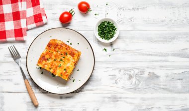 Eritilmiş peynirle kaplı ve gri tabakta servis edilen taze maydanozla süslenmiş kıymalı lazanya porsiyonu. Üst Manzara. Metin için boşluk