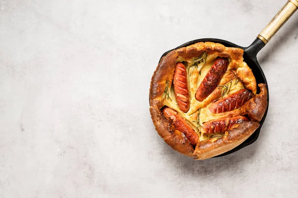 Toad in the hole, Sausage Toad, traditional English dish of sausages in Yorkshire pudding batter. Light gray background, top view. Space for text