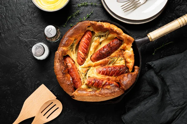 Toad in the hole, Sausage Toad, traditional English dish of sausages in Yorkshire pudding batter. Black background, top view