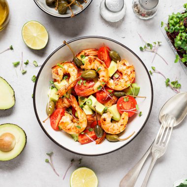 Kolay ızgara karides avokado salatası, vişneli domates, kapari ve mikroyeşillik. Gri arka plan. Üst görünüm.