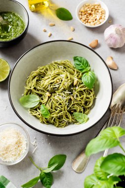 Pesto soslu makarna ve gri kasede taze fesleğen yaprağı. Açık gri arkaplan. 