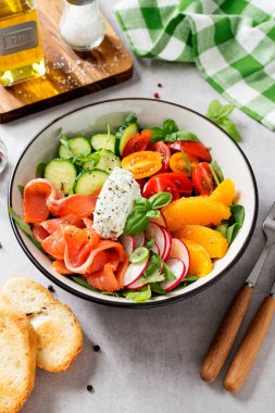 Ispanaklı somon kasesi, roka, kiraz domatesleri, salatalık, portakal dilimleri, turp ve krem peyniri. Ev yapımı yemek. Lezzetli ve sağlıklı bir yemek konsepti. Açık gri taş arkaplan. 