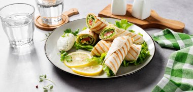 Sandviç paketle, tuzlanmış somon balığı ve taze sebzelerle yuvarlan. Açık gri arkaplan.