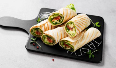 Sandviç paketle, tuzlanmış somon balığı ve taze sebzelerle yuvarlan. Açık gri arkaplan.