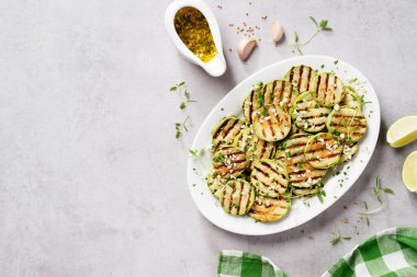 Beyaz tabakta sarımsak soslu ızgara kabak dilimleri. Açık gri taş arka plan. Üst görünüm.