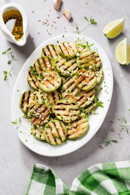 Beyaz tabakta sarımsak soslu ızgara kabak dilimleri. Açık gri taş arkaplan. 