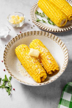 Parmesan peyniri, tuz ve tereyağı ile servis edilen koçandaki mısır. Açık gri arkaplan.