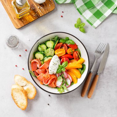 Ispanaklı somon kasesi, roka, kiraz domatesleri, salatalık, portakal dilimleri, turp ve krem peyniri. Ev yapımı yemek. Lezzetli ve sağlıklı bir yemek konsepti. Açık gri taş arka plan. Üst görünüm.