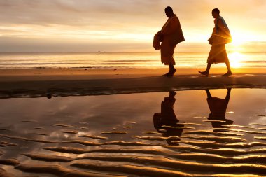 Silhouettes of monks on Hua Hin beach Thailand clipart