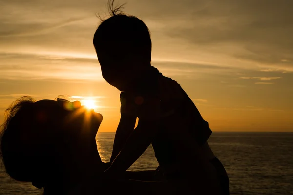 Matka i trochę sylwetki syna na plaży o zachodzie słońca — Zdjęcie stockowe