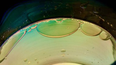 Sıvı bir yüzeyde yüzen yağ küresi renkli soyut desenler oluşturur