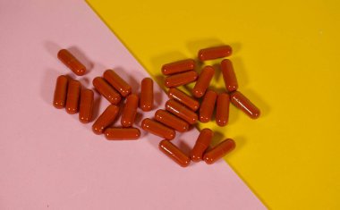 Pembe ve sarı yüzeye dağılmış kırmızı tıbbi kapsüller.