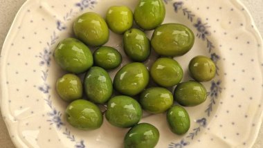 Mavi çiçekli ve benekli beyaz bir seramik tabakta duran yeşil zeytinler.