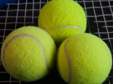Üç parlak sarı tenis topu siyah tenis raketinde maç bekliyor.