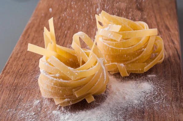 Raw tagliatelle with flour on brown wooden table — Stock Photo, Image