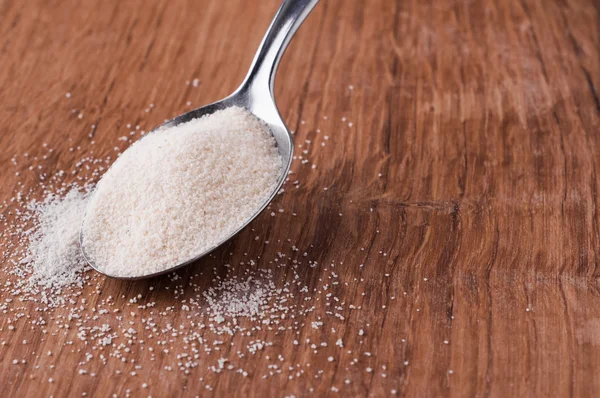 Semolina on metal spoon on brown wooden table — Stock Photo, Image