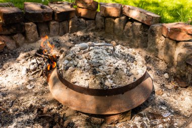 Photo of Cooking traditional dalmatian, croatian, bosnian dish called peka. Meat, potatoes and vegetables in pot and covered with hot charcoal and ash. Balkan food.