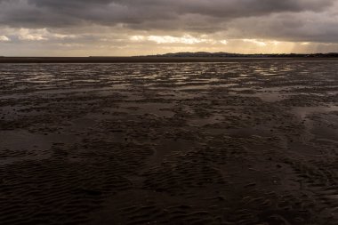 Sandymount Sahili, Dublin, İrlanda 'da dramatik ve karamsar bir atmosfer. Islak gelgit düzlüklerinin geniş ön planı karanlık ve fırtınalı bulutları yansıtır. Işık uzak ufukta beliriyor. 