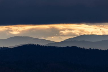 Polonya, Beskidy 'deki sisli dağ sırtlarının fotoğrafları, dramatik bir karanlık gökyüzünün altında, altın bir gün batımı çizgisi parlıyor..