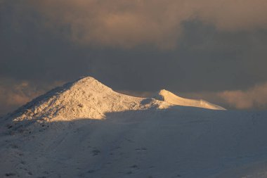 Bieszczady Dağları 'ndaki Polonina Wetlinska' nın kış zirvesi, gün batımında altın güneş ışığı, karla kaplı dağ zirvesine vuruyor, kara dramatik bulutlara karşı, Polonya 'da güzel kış manzarası, fotokopi uzayı. Bieszczady Ulusal Parkı.
