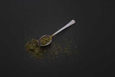 Üzerinde koyu ahşap masa üzerinde metal çay kaşığı kuru fesleğen