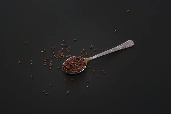 Linseed on metal spoon on dark wooden table — Stock Photo, Image