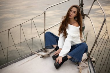 Gün batımında beyaz kazaklı genç bir kız bir yatta dinleniyor.