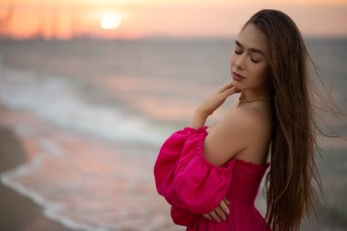 Pembe elbiseli genç kız gün doğumunda deniz kıyısında yürüyor.