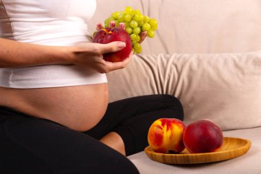 Hamile bir kadın elinde meyve tabağıyla kanepede oturur. Yüksek kalite fotoğraf