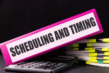 SchedULing ve MITing metni bir ofis masasındaki kağıt yığınının üzerinde duran bir klasöre yazılmıştır. İş konsepti.