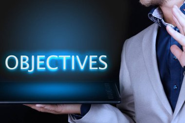 İş adamı, elinde neon bir kelime olan bir tablet tutuyor, OBJECTIVES metni. İş konsepti.