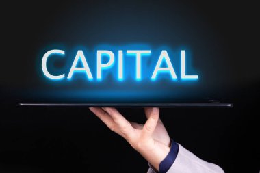 İnsan eli üzerinde neon bir metin yazan bir tablet tutar, CAPITAL kelimesi. İş konsepti.