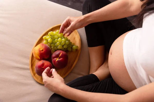 Hamile Bir Kadın Elinde Meyve Tabağıyla Kanepede Oturur Yüksek Kalite — Stok fotoğraf