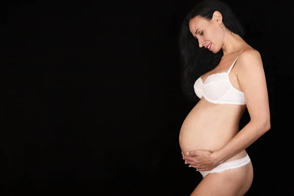 Uma Mulher Grávida Fica Lingerie Branca Fundo Preto Segura Sua — Fotografia de Stock