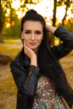 Koyu renk saçlı güzel bir kadının portresi, yaz günbatımının arka planında bir kız ve yeşil bir park.